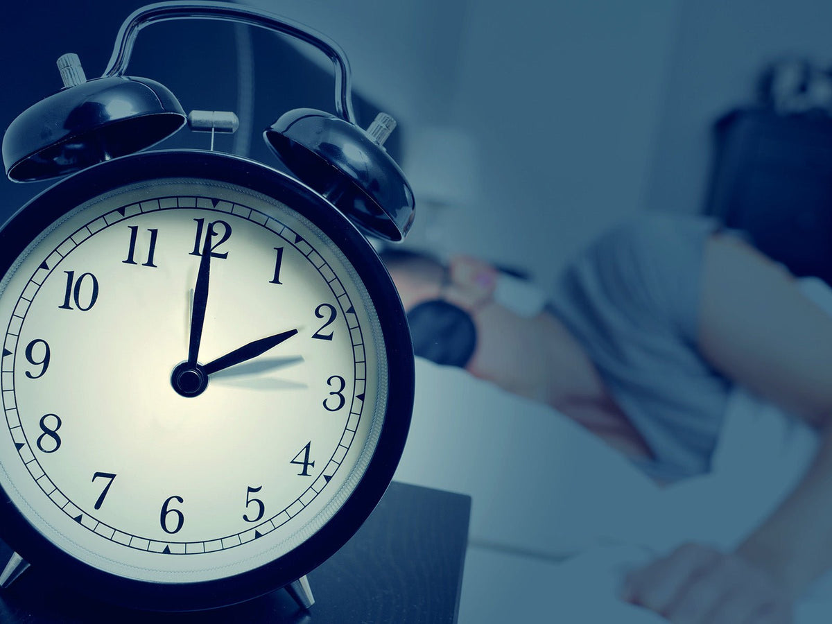 Alarm clock beside a bed illustrating recommended sleep duration and healthy sleep habits