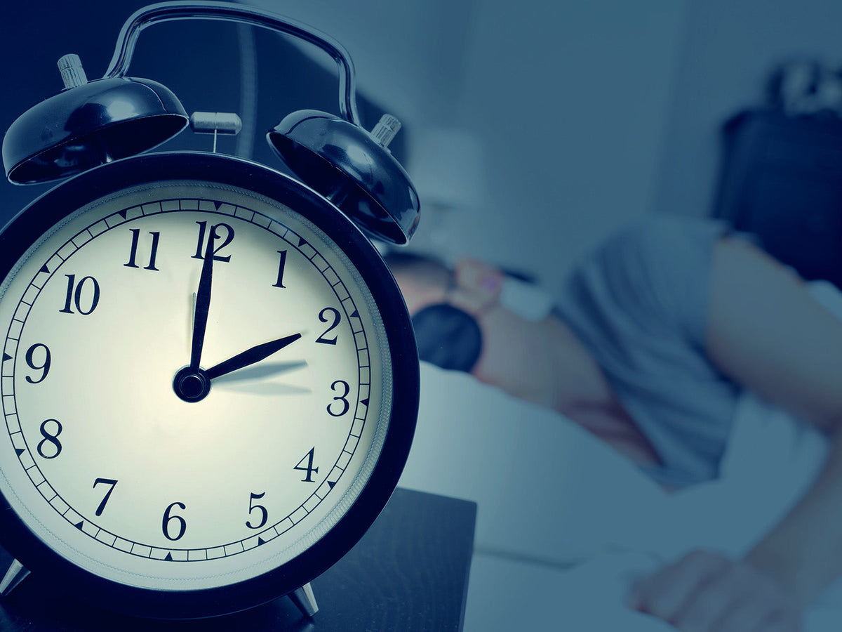 Alarm clock beside a bed illustrating recommended sleep duration and healthy sleep habits