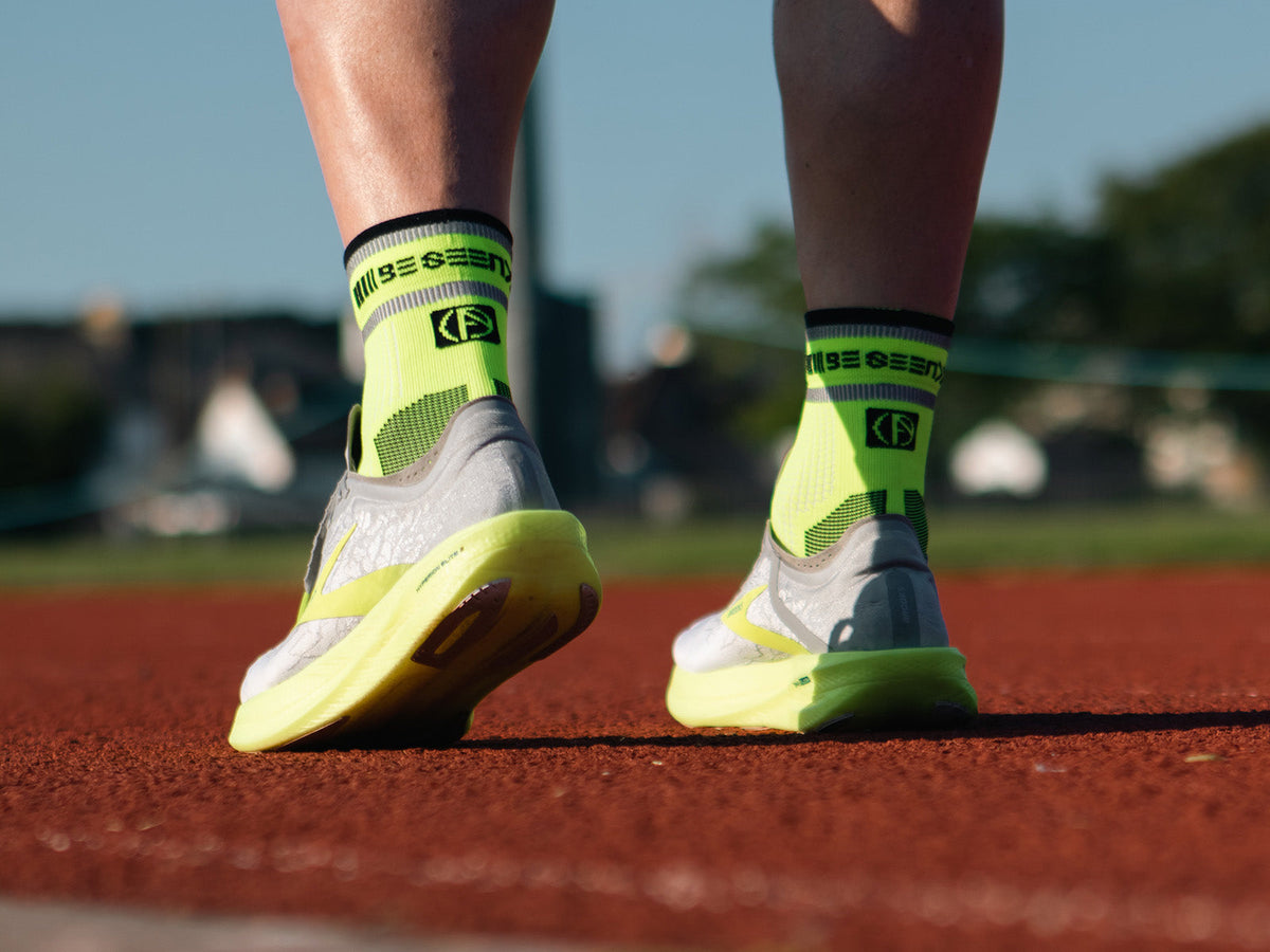 Runner wearing neon yellow ABSOLUTE360 running socks on a running track
